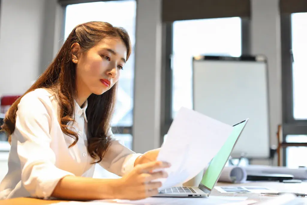 Woman reading through printed papers in an office with warm grey walls